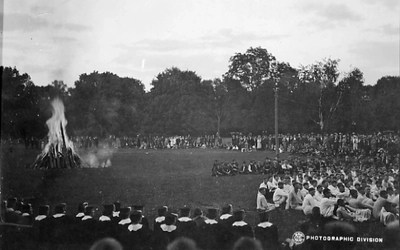 Students sitting around a bonfire on Cap Night wearing beanies or caps and gowns.
