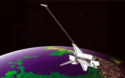 An illustration shows the Space Shuttle orbiting Earth with a long radar antenna extending into space during a mapping mission.