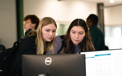 Two students leaning in to look closely at a "Roommate Group Membership" screen on a Dell monitor.