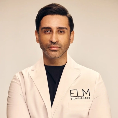 Portrait of Dhaval Bhanusali in a white medical lab coat with a patch that reads ELM Biosciences