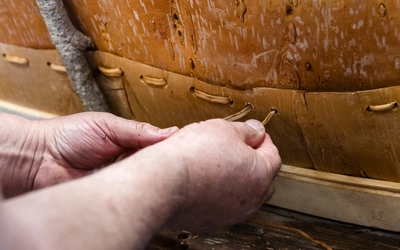 Close-up of a person stitching birch bark together while building a traditional canoe and sharing Ojibwa cultural traditions.