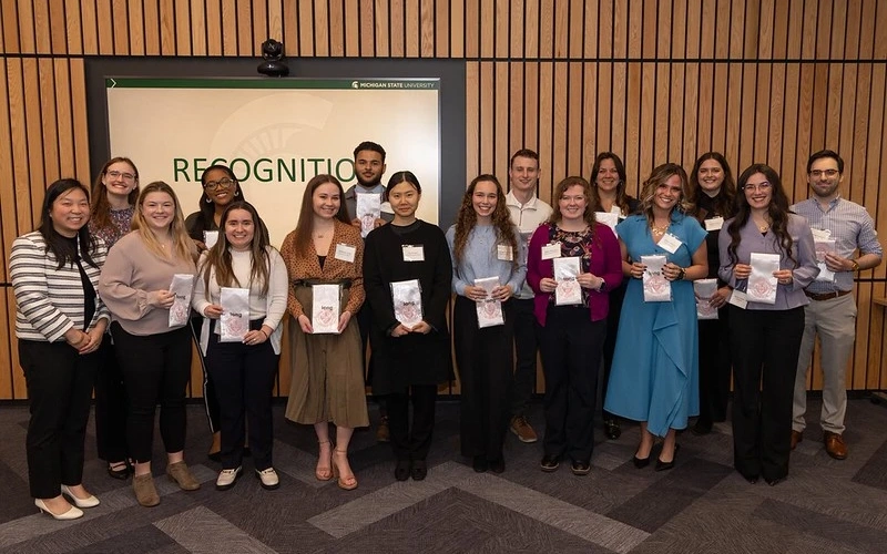Students pose for a picture while holding awards in front of a screen with "Recognition."
