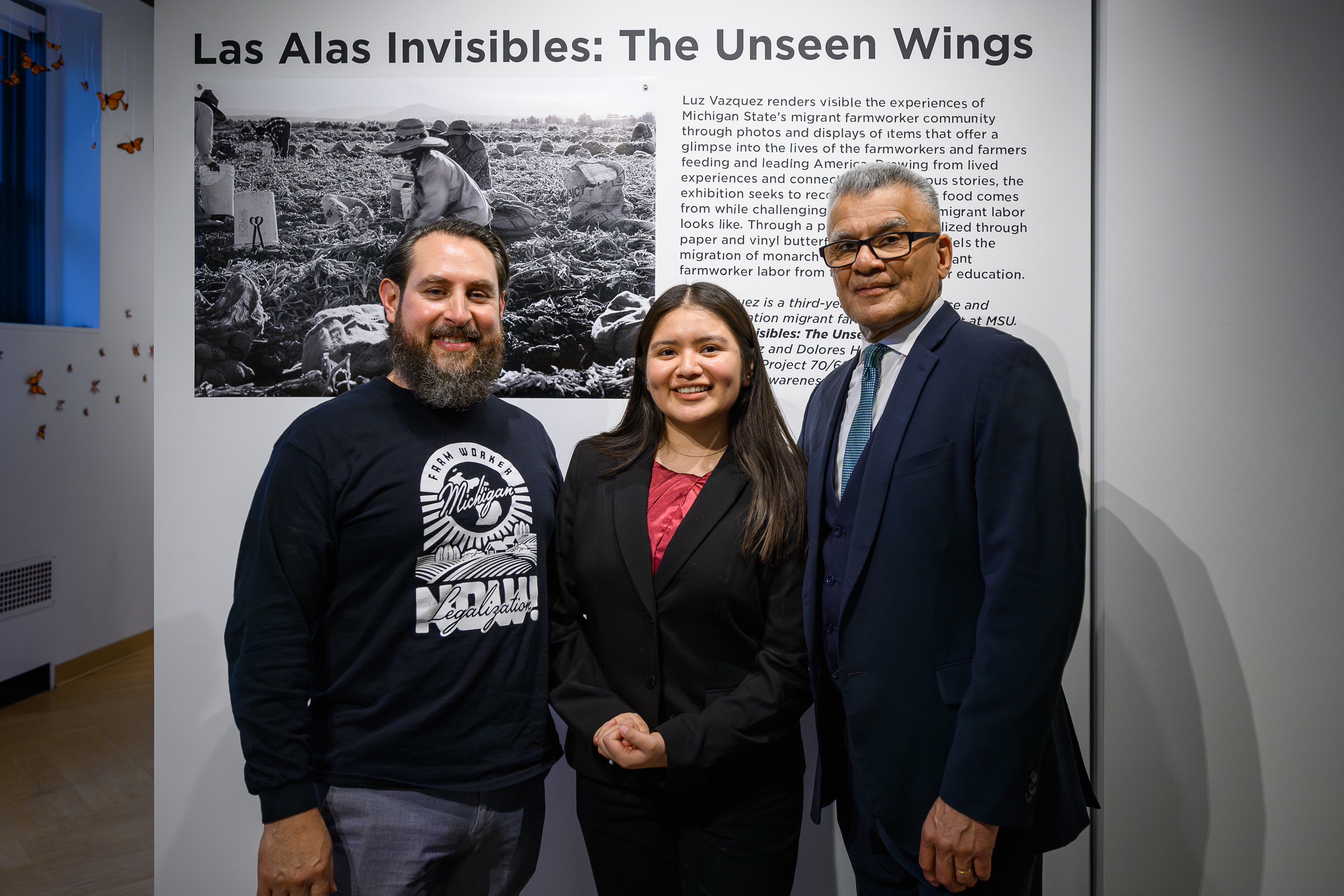 Three people stand in front of an exhibition signage