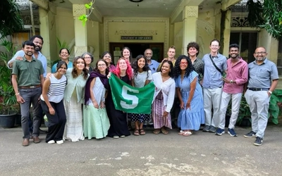 MSU students and faculty hold a green Spartan flag while posing outside the Department of Crop Science during their study abroad program in Sri Lanka.