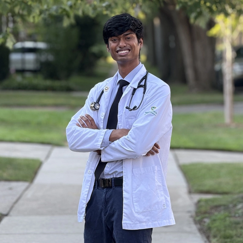 Hari Ramakrishnan smiles while wearing a medical white coat and stethoscope around his neck.
