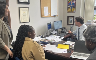 Students sit around the desk of the director of a law clinic at his desk inside the building of the MSU College of Law.