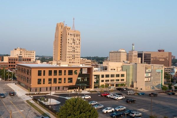 A view of downtown Flint, Michigan, featuring the historic Mott Foundation Building surrounded by other mid-rise buildings, a parking lot in the foreground, and the Michigan State University College of Human Medicine public health building with a Spartan helmet logo."