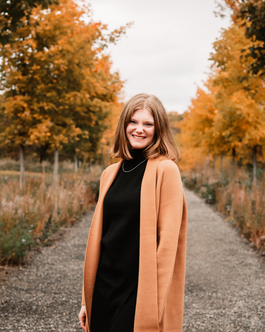 A woman standing outdoors with fall trees