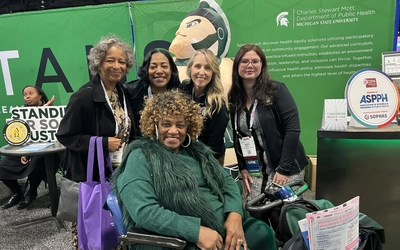 Group of people smiling together in front of an MSU Department of Public Health banner.