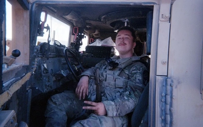 Liam McDonald posing in the driver's seat of a military car during training.