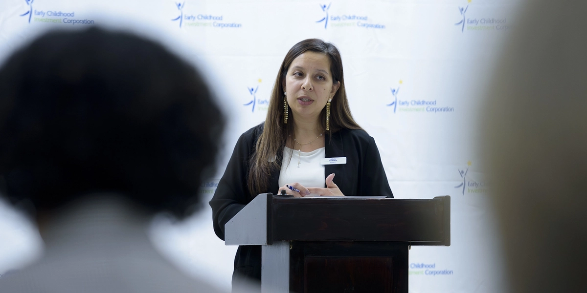 A woman stands at a podium speaking to audience.