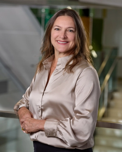 Professional headshot of Dr. Jennifer McCurdy, smiling with shoulder-length brown hair, wearing a dark top and a light-colored blazer, set against a neutral, softly lit background.