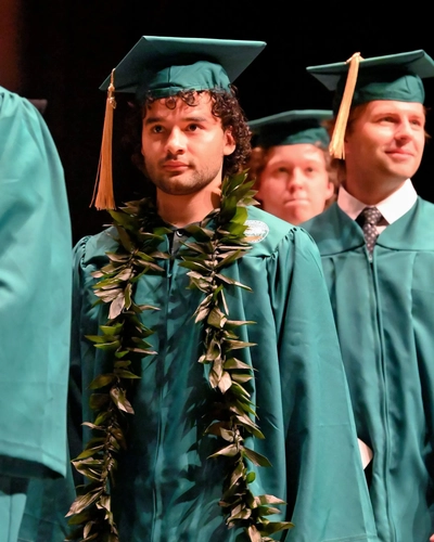 A man wearing a lei is walking on stage at graduation