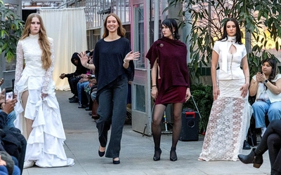 Designer Evelyn Short standing and waving to a clapping crowd on a runway next to three models wearing her designs.