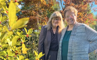 Rebecca Lehto and Gwen Wyatt pose in front of greenery