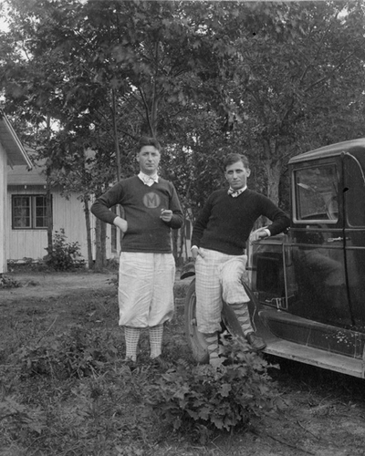 Two young men stand next to an old truck in 1947