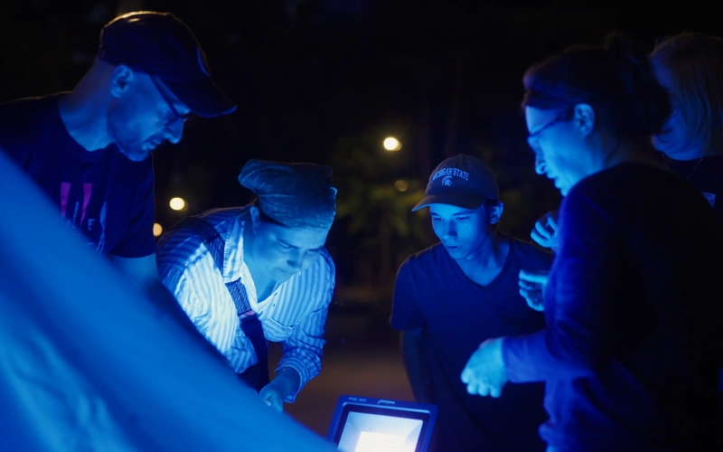 Group of people huddle around a glowing blue light source for event installation.
