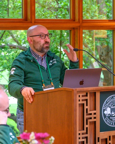 Man in glasses stands behind MSU podium giving remarks.