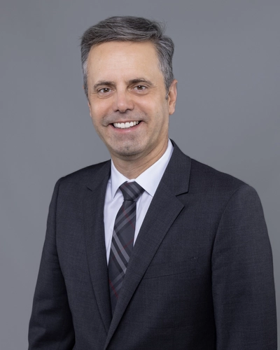 Marcio A. Oliveira smiles in a studio portrait wearing a dark suit and tie.