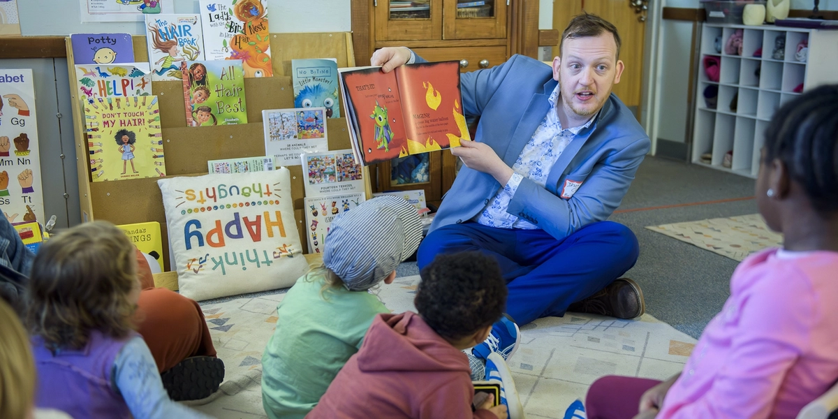 An adult reads a book to young children.
