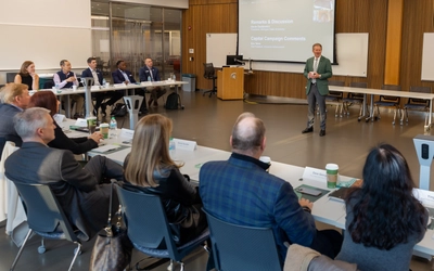 A person stands in front of a group of people sitting at tables facing him.