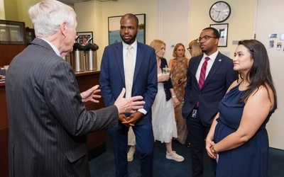A group of people, including a senator, speak inside an office as others listen and observe.