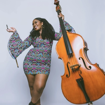 Musician Endea Owens posing enthusiastically with a double bass in front of a white studio backdrop.