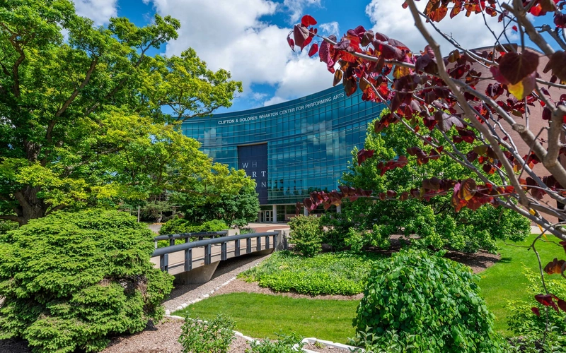 Clifton and Dolores Wharton Center for the Performing Arts seen behind green trees and flowers.