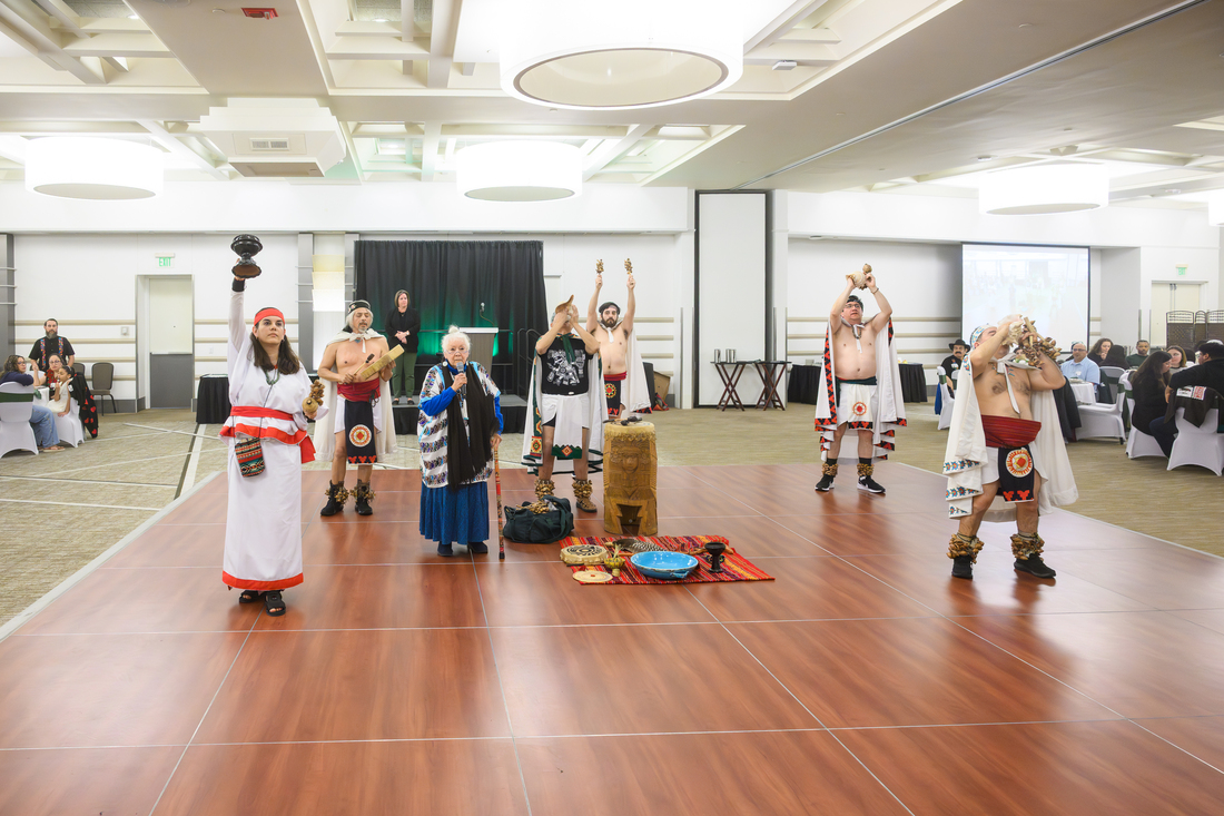 Indigenous ceremonial opening with seven people on a stage holding various items