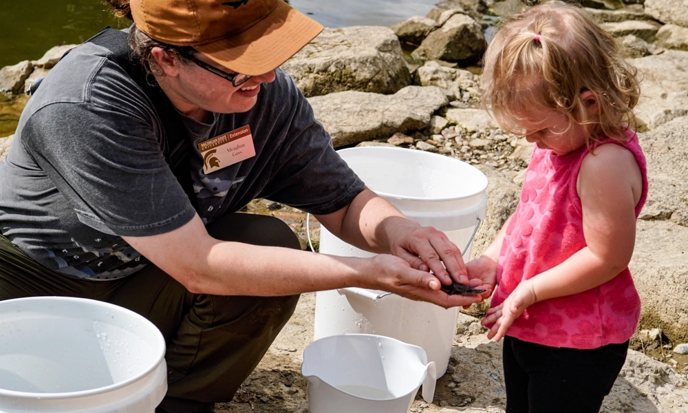 A person holds a small sturgeon, showing it to a young child