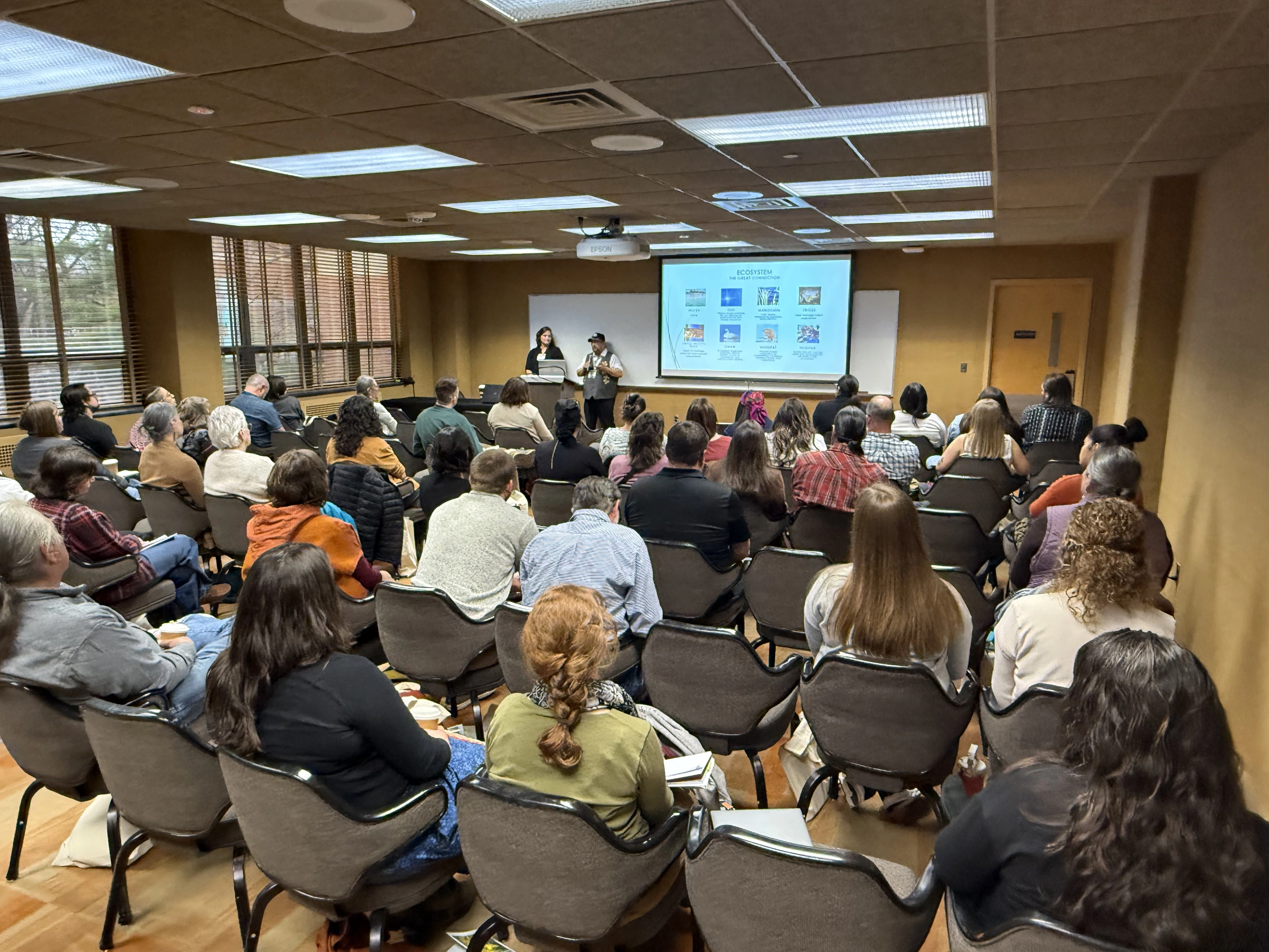 Full session of attendees seated facing the presenters at the front of the room