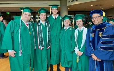 Will Castanier smiling with four other graduates at JMC's Spring 2026 Commencement Ceremony.