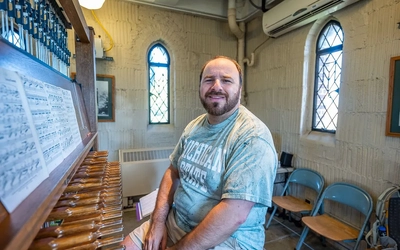 Jonathan Lehrer sits smiling in Beaumont Tower at a seat in front of the tower's carillon.