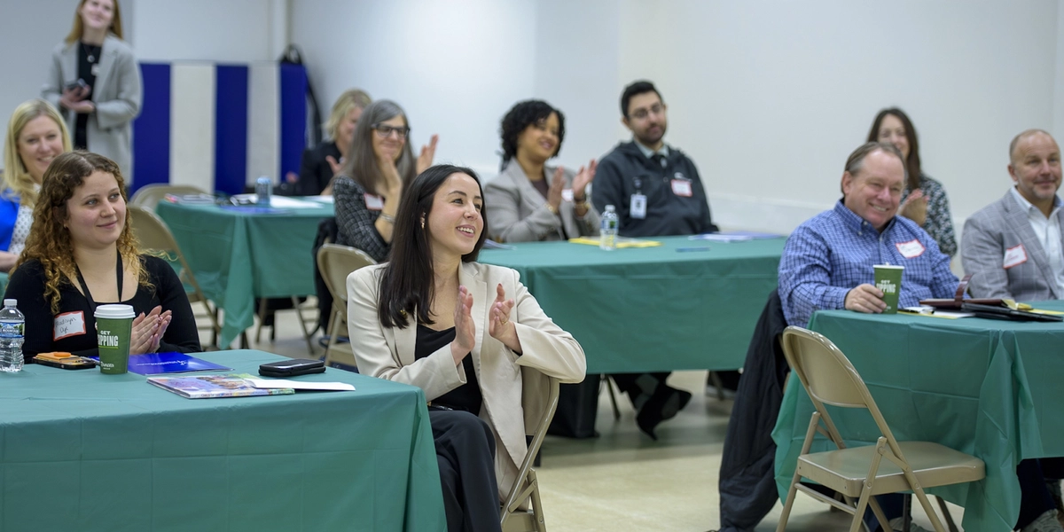 People seen sitting around tables clap as they attend an event for promoting the development of children.