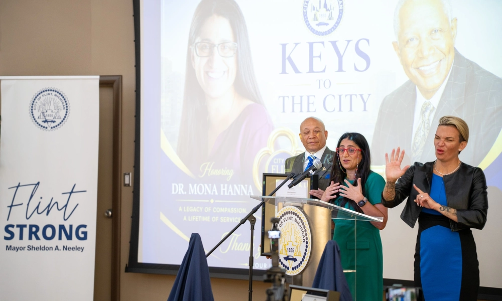 Dr. Mona Hanna-Attisha standing on stage at a podium while receiving a Key to the City award during a ceremony in Flint.