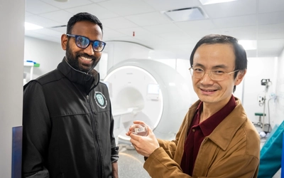 Chunqi Qian, right, holds a small wireless sensor while standing with a colleague in front of an MRI scanner.
