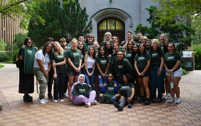 A group of students from the EXCEL Bridge Program standing outside Beaumont Tower. They are all wearing green shirts