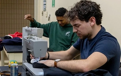 Tony Cox and Fernando Caccia finishing their designs for the fashion show. Caccia uses a sewing machine.