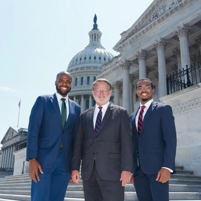 Three men in suits stand on the steps of the U.S. Capitol building.