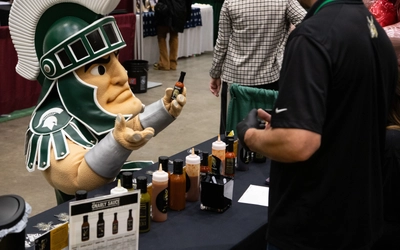 Sparty mascot shows off a hot sauce bottle at an event