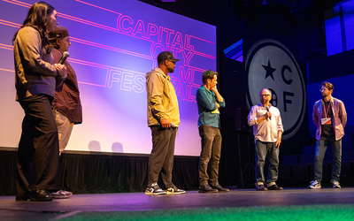 Six people stand on stage talking with a crowd about films and filmmaking. In the background are the words “Capital City Film Festival” and a circle logo that says “CCFF.”