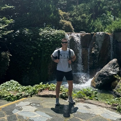 Student Colt Gray stands on a stone patio in front of a waterfall feature during a hike in Seoul in summer 2026.