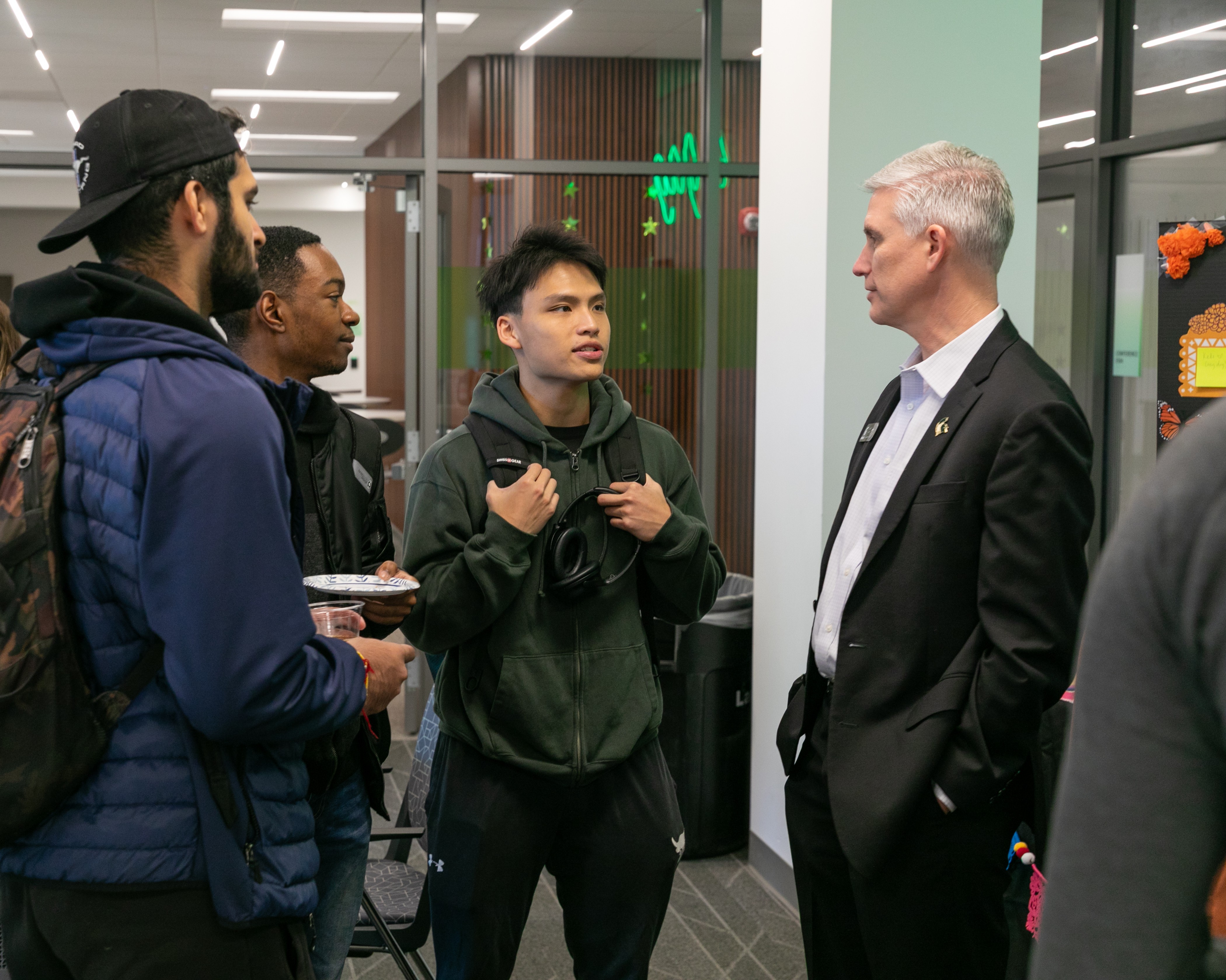 A group of students stand around in conversation with a professionally dressed man