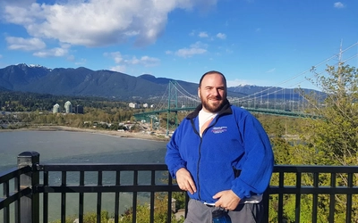 Jonathan Lehrer standing smiling in front of a body of water and bridge in Vancouver.