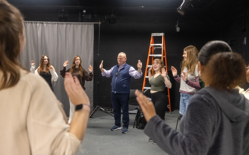 A group of people stand in a circle with their hands up, palms facing the other person.