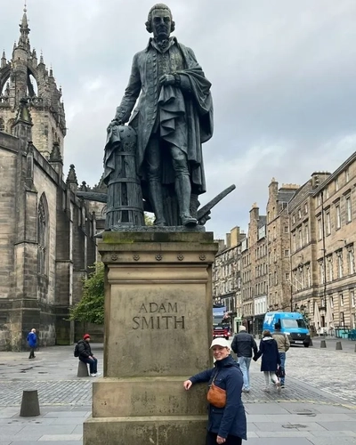 Prof. Brianne Wolf smiling and leaning on a statue of Adam Smith in Scotland during a fall 2023 trip to visit the University of Edinburg’s Smith archive.