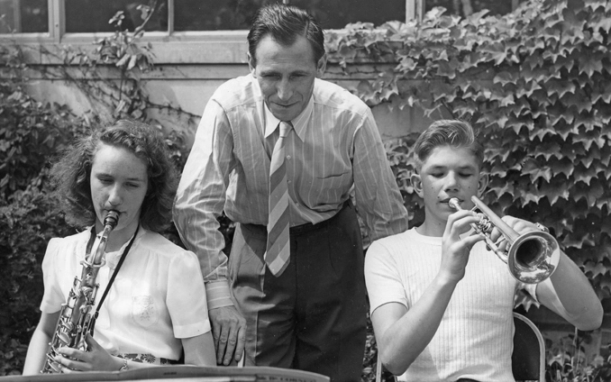 Two students playing a saxophone and trumpet are instructed by Leonard Falcone