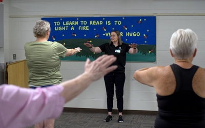 MSU Extension health educator extends arms, showing participants tai chi method
