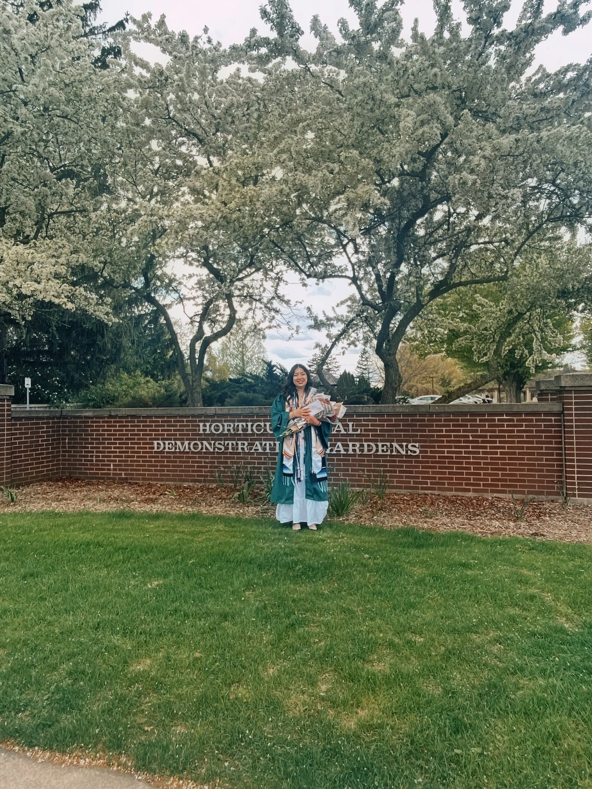 A student stands with graduation gown holding a bouquet