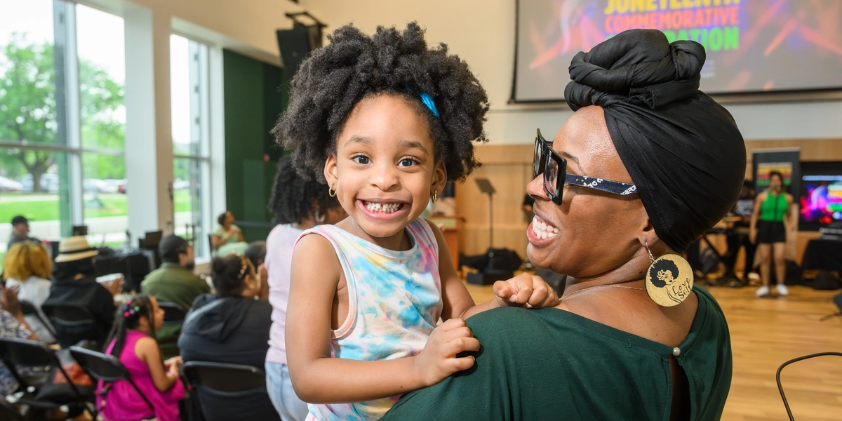 A woman carriers a young child who is smiling